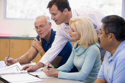 Professor leans over mature students to look at a research file