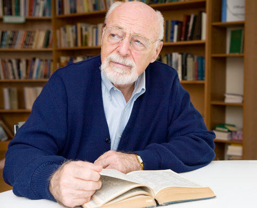 Senior man thinking about the book he is reading in the library.